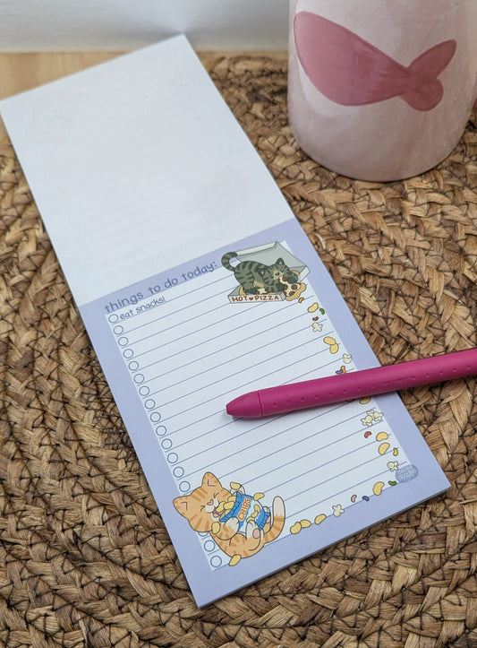 Notepad with cat illustrations, pen, and mug on a textured surface
