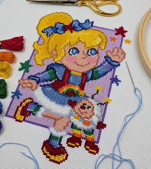 Cross-stitching project with a colorful character and rainbow-themed design.