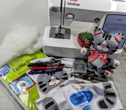 Sewing machine and sewing supplies laid out on craft table. Completed stuffed cat included.