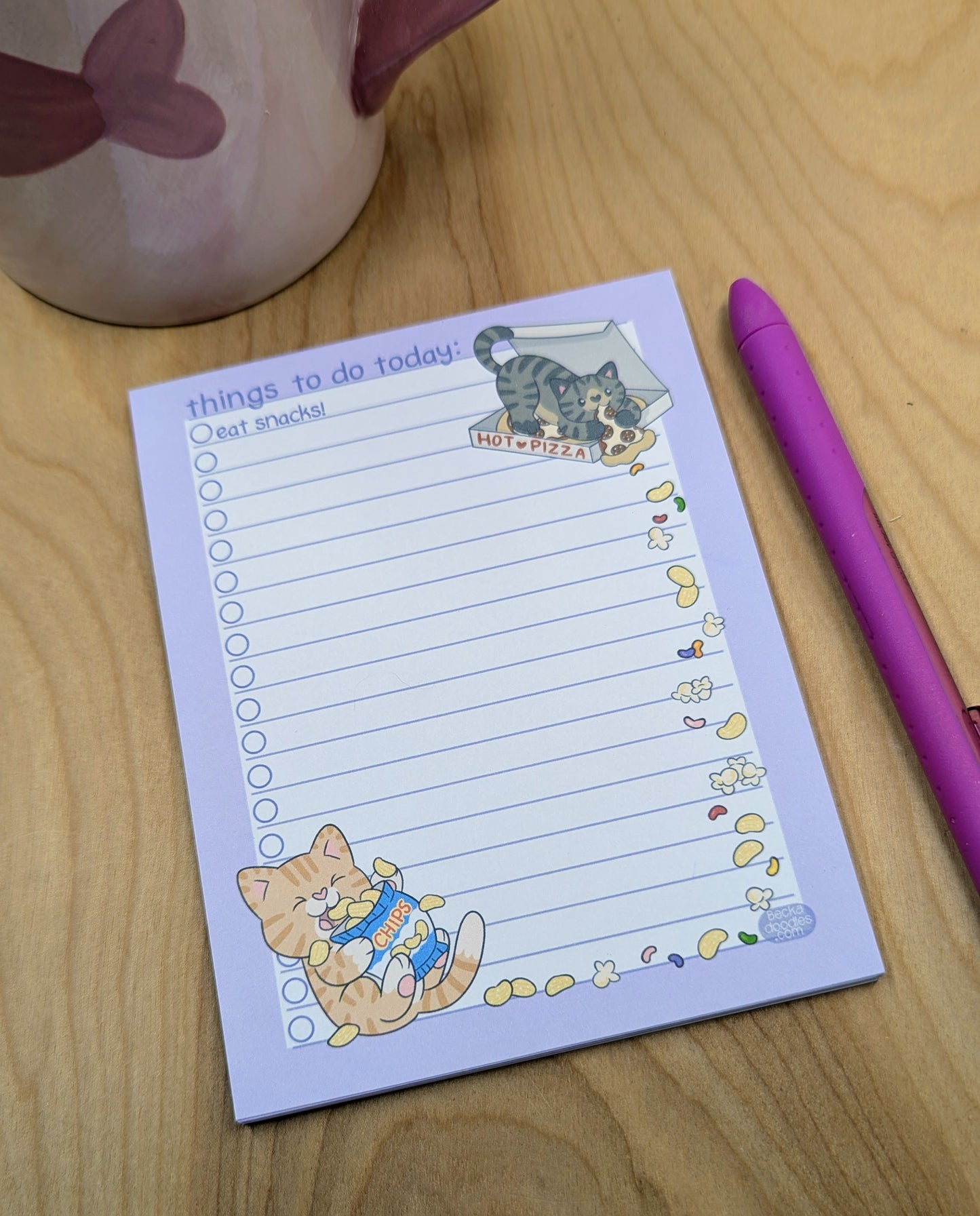 Notepad with cat illustrations and a pen on a wooden surface