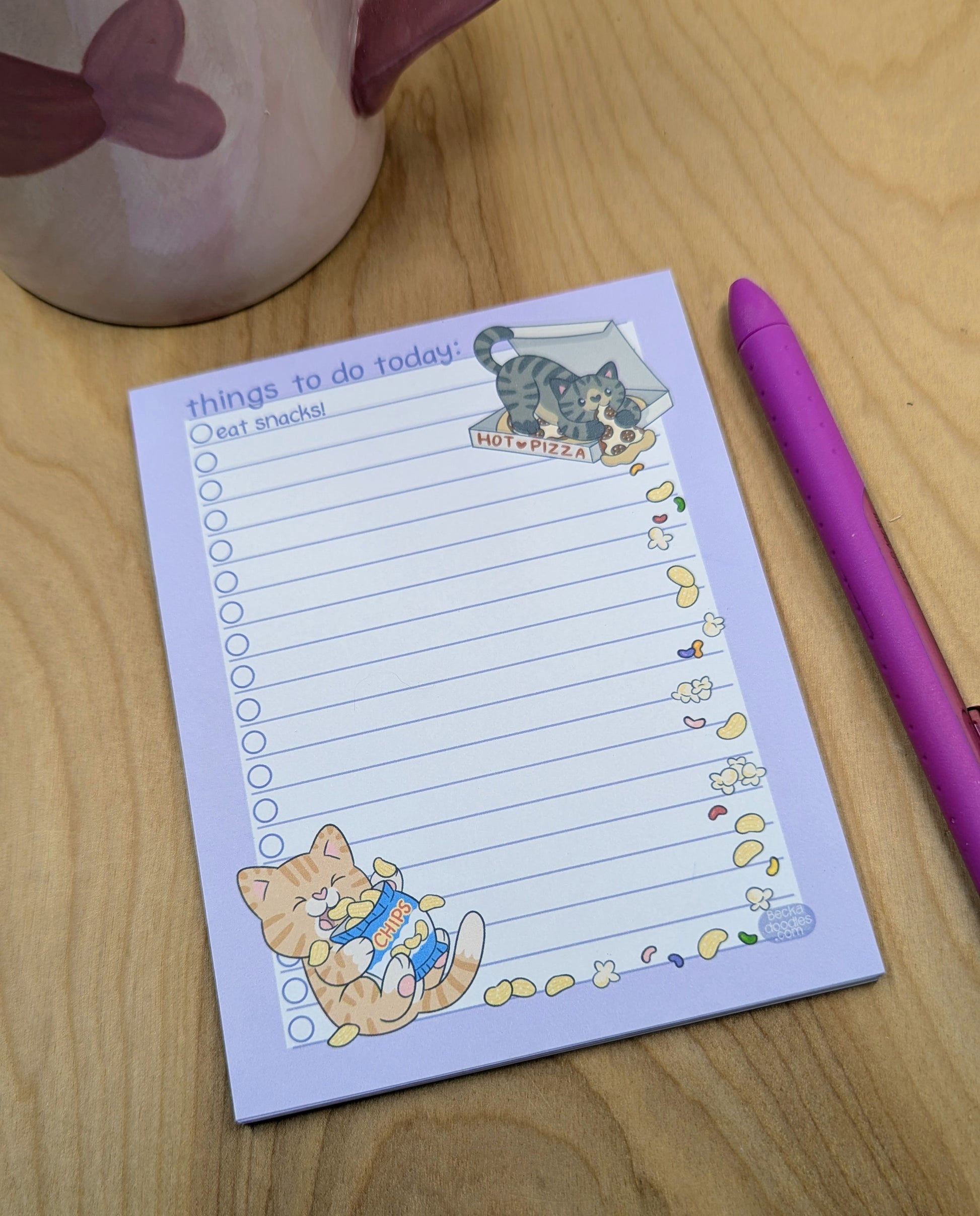 Notepad with cat illustrations and a pen on a wooden surface