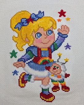Cross-stitched design of a girl with a rainbow and stars on a white background