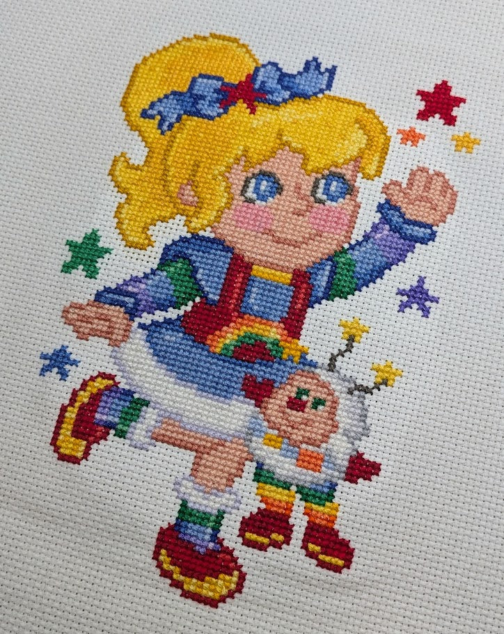 Cross-stitched design of a cartoon character with colorful attire and accessories on a white background.