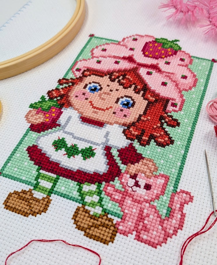 Cross-stitched design of a character with a pink hat and a cat on a white background