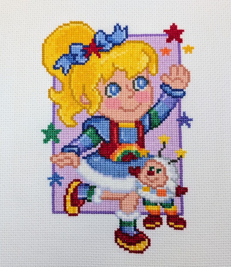 Cross-stitched design of a girl with a rainbow-colored dress.