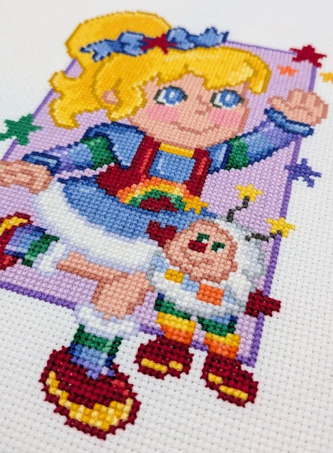 Colorful cross-stitch pattern of a cartoon girl with rainbow-themed elements.