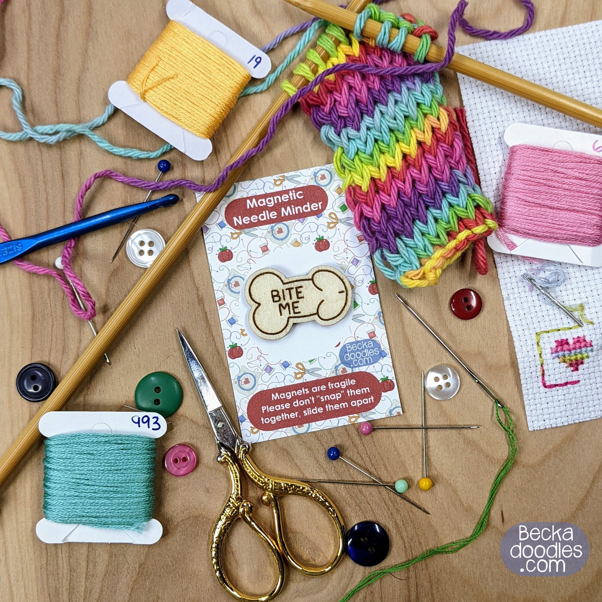 Crafting supplies including yarn, needles, and a Magnetic Needle Minder on a wooden surface.