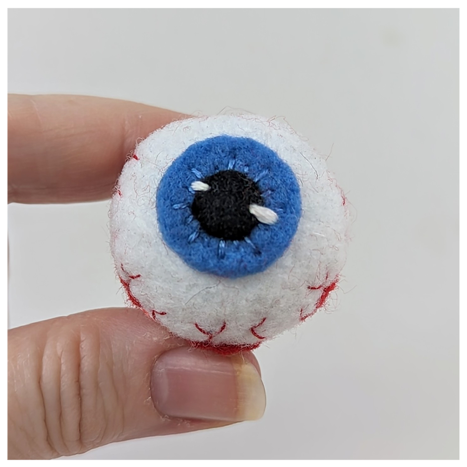 Felted eye held between fingers against a plain background