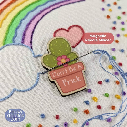 Magnetic needle minder shaped like a cactus with a humorous message on embroidery fabric.