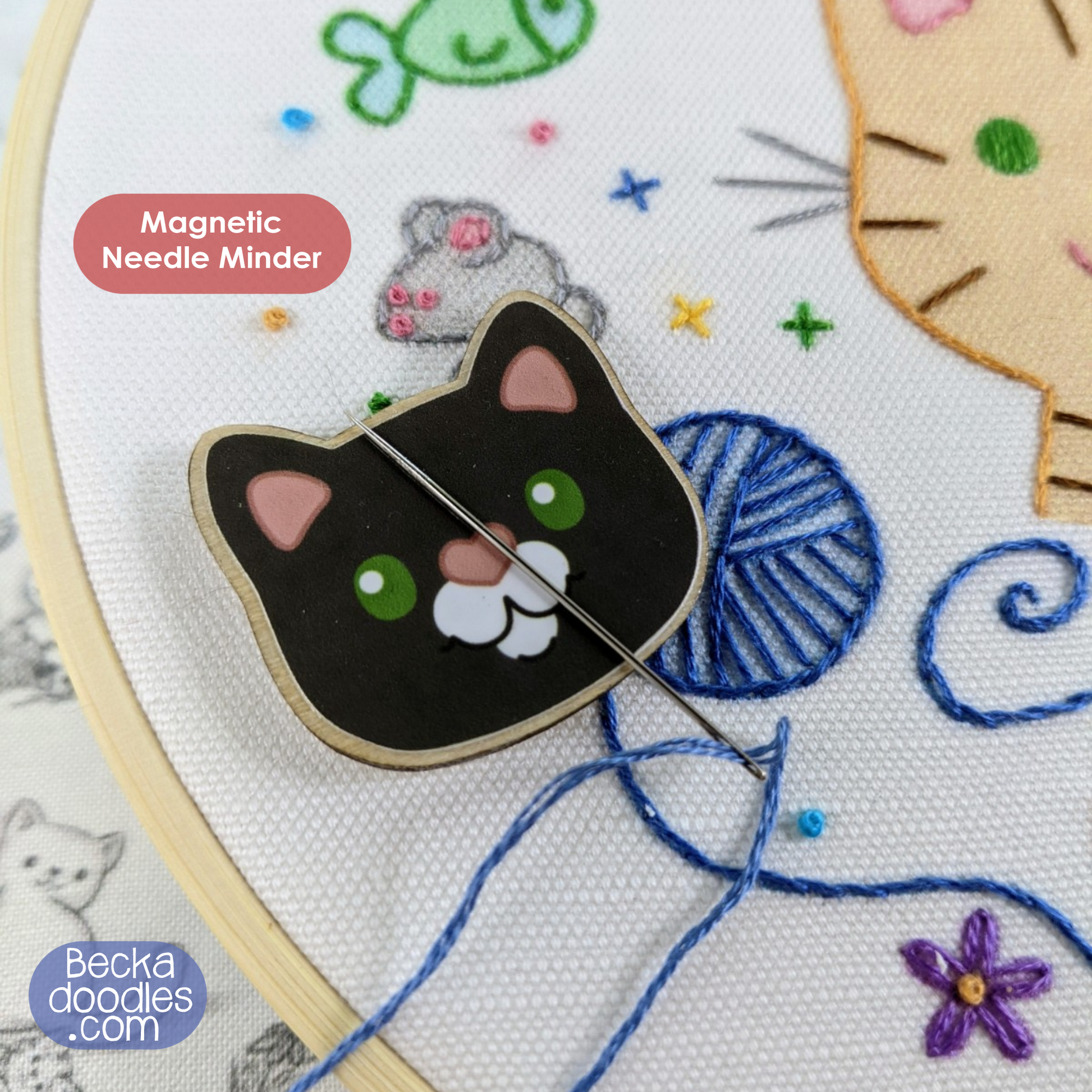 Cat-shaped magnetic needle minder on an embroidery hoop with colorful thread and designs.