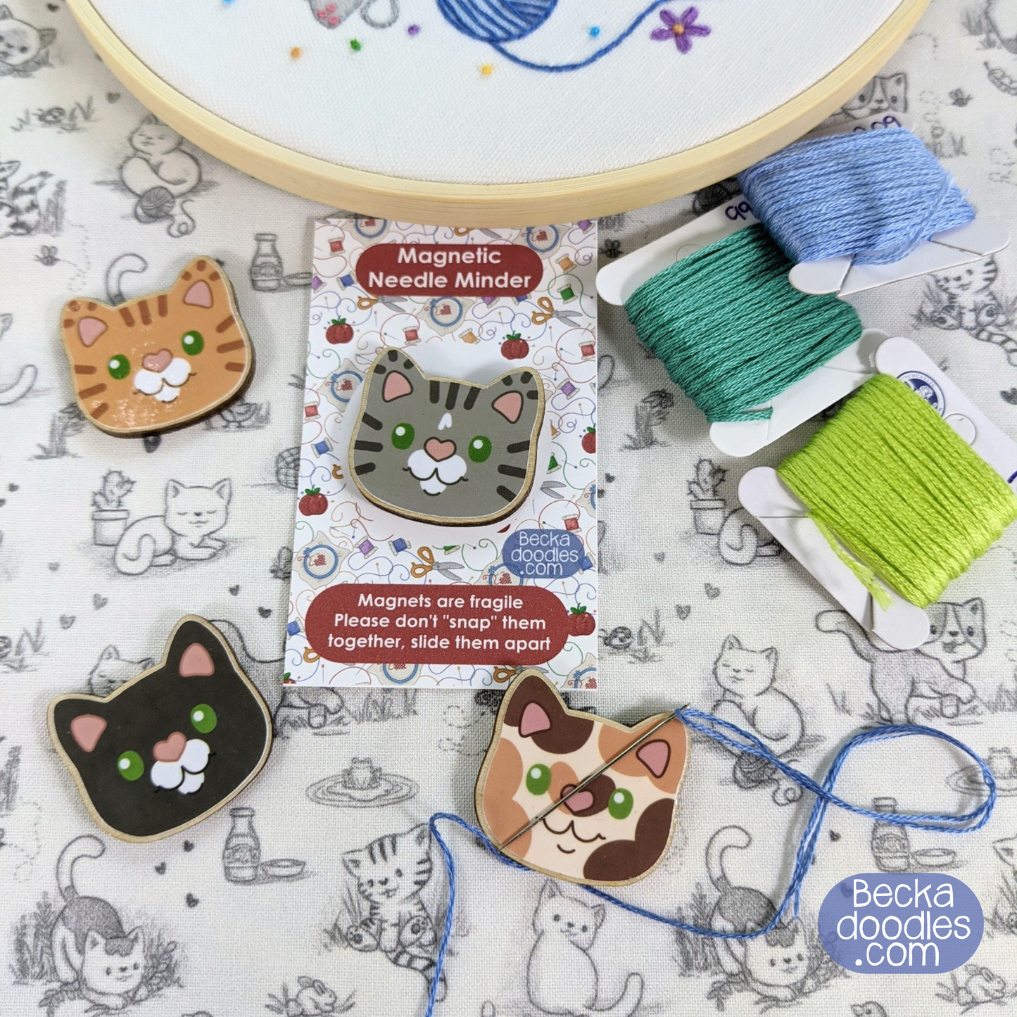 Cat-themed magnetic needle minder with packaging on a patterned background