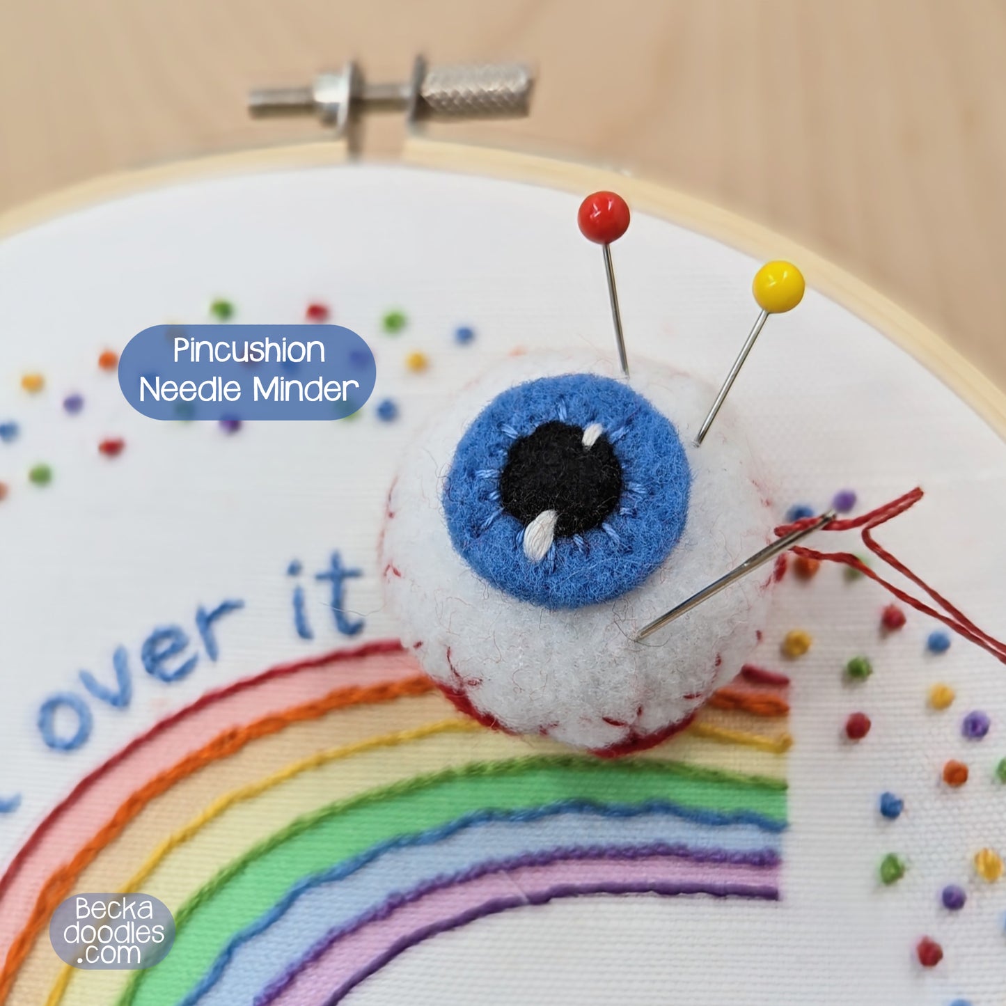 Embroidery hoop with rainbow design and pincushion needle minder, featuring 'Becka Doodles' branding.