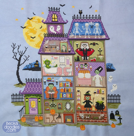 A cross-stitch design of a haunted house with Halloween-themed rooms, skeletons, a vampire, ghosts, pumpkins, bats, and a large yellow moon on a pale blue fabric. 