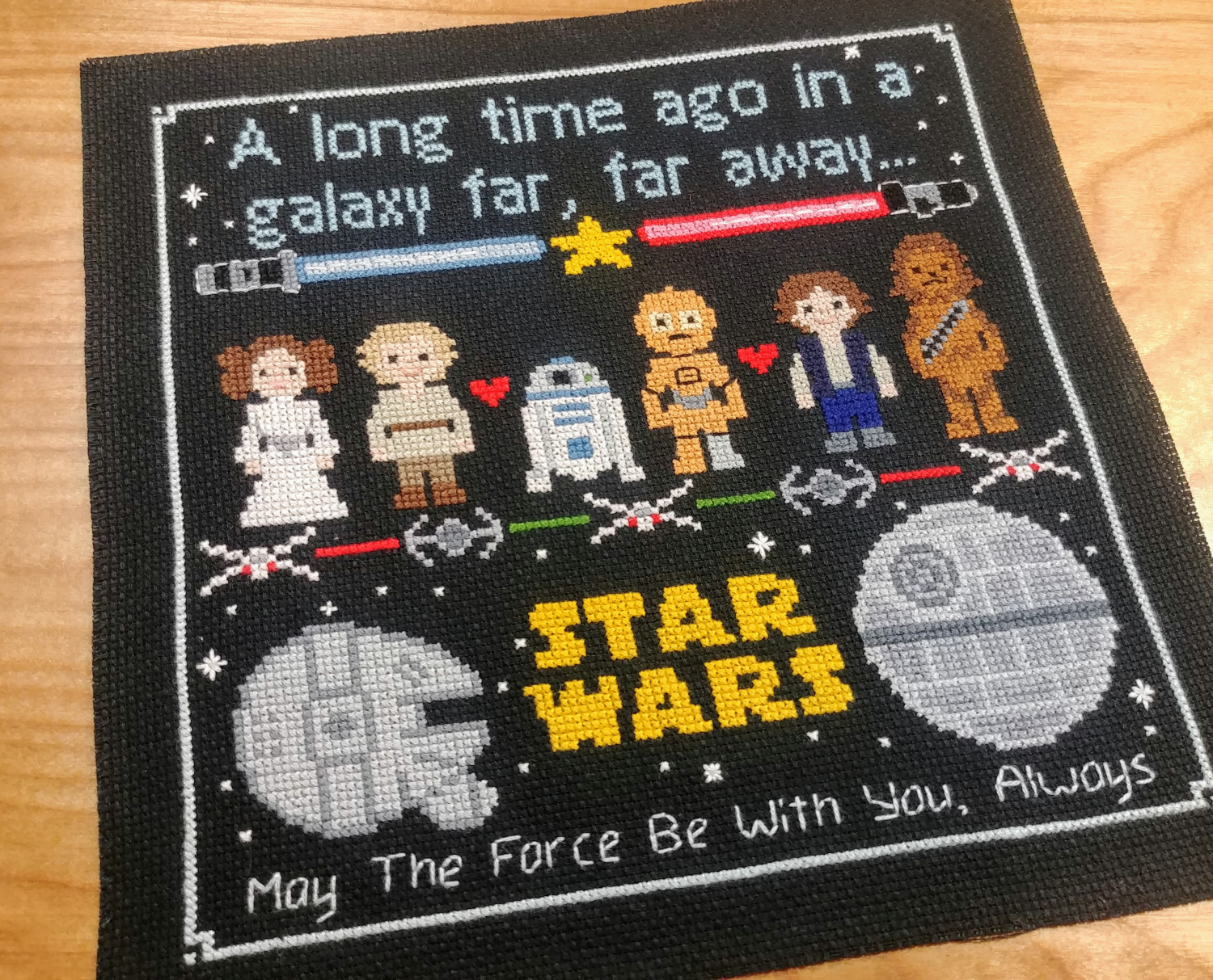 Science-fi-themed cross-stitched panel with characters and text on a wooden surface.