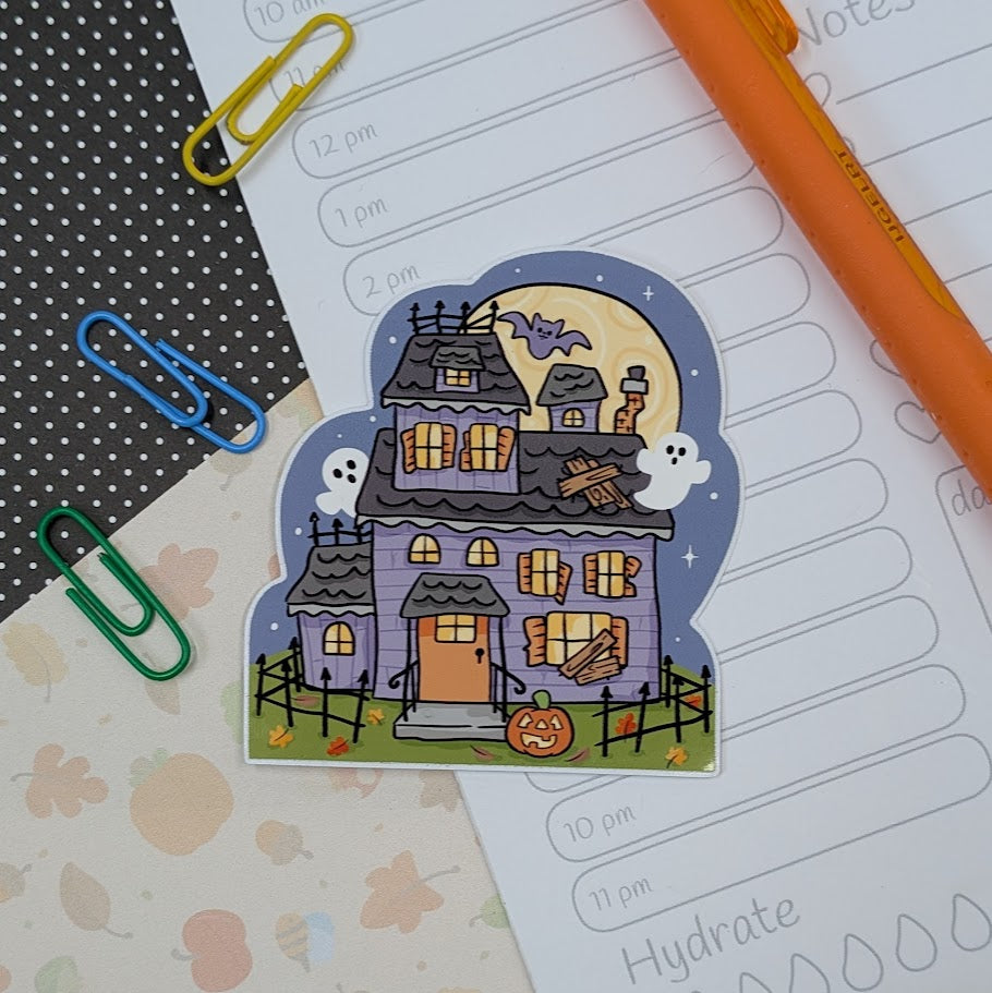 Halloween-themed house sticker on a planner with colorful paper clips and a pen.